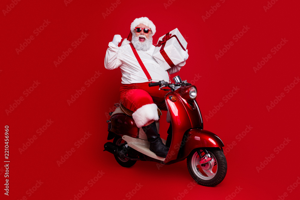 Obraz premium Santa Claus on a red scooter delivering a wrapped gift with festive cheer and sunglasses, energetic holiday concept for Christmas celebration and seasonal delivery