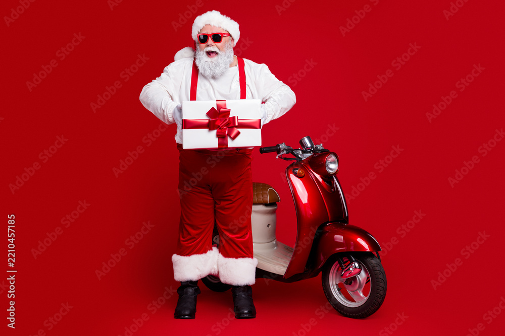Obraz premium Santa Claus holding a wrapped gift next to red scooter in festive Christmas scene with sunglasses and joyful holiday spirit