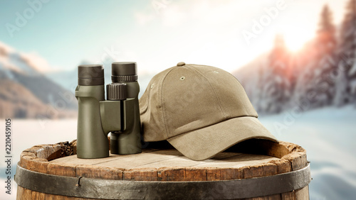 Binoculars on a rustic wooden barrel with softly blurred snowy mountain, winter landscape background, Scenic winter atmosphere, outdoor adventure, travel, nature exploration and mountain tourism.