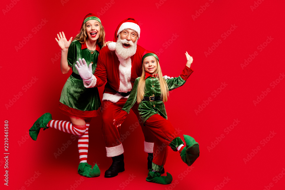 Obraz premium Santa and two cheerful elves posing together in festive Christmas costumes against a bright red background for holiday family fun and seasonal celebration