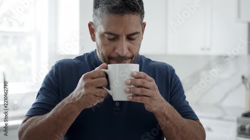 Man in shirt drinking hot coffee from white cup in bright kitchen