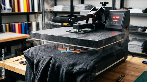 Heat press machine applying vinyl graphic to dark gray hoodie in workshop