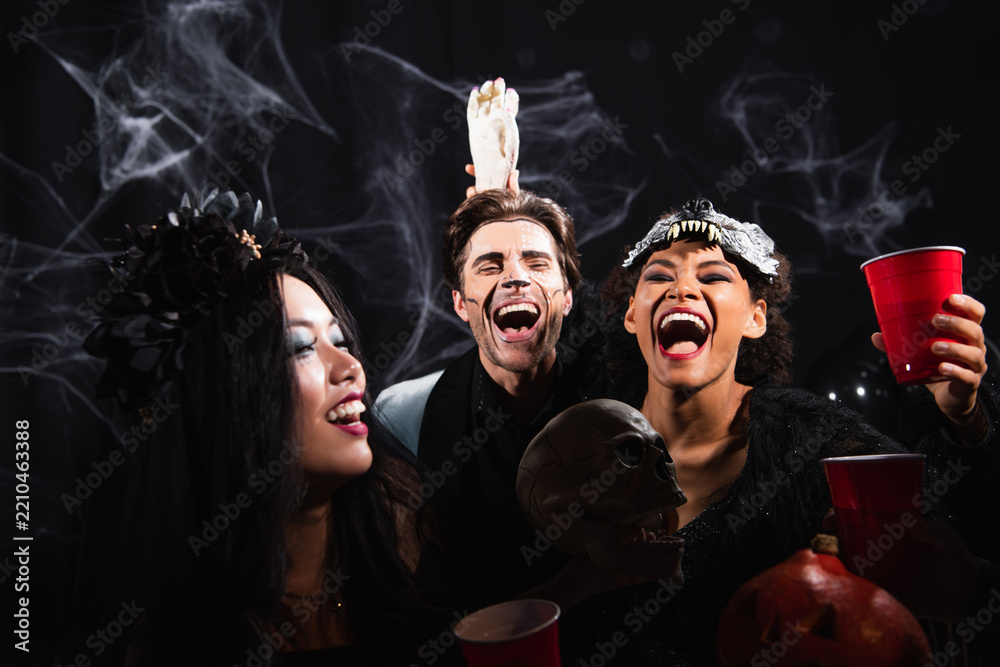 Obraz premium Multicultural friends joyfully celebrate Halloween with drinks at a costume party