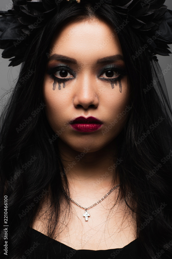 Fototapeta premium Young woman embraces spooky elegance in witch makeup and floral crown