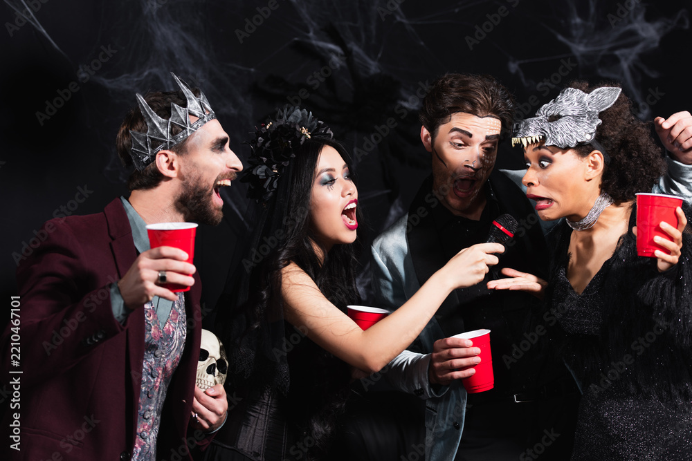 Obraz premium Multicultural friends enjoying a lively Halloween costume party celebration with karaoke 
