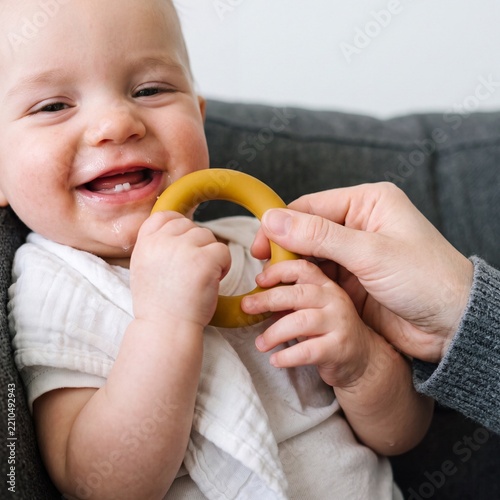 Teething baby laughing with first tooth and yellow teether