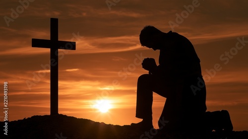 Silhouette of a man kneeling in prayer before a wooden cross at sunset