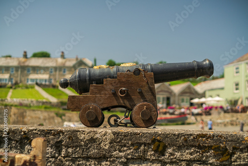 View of an antique cannon on a wooden carriage resting on a stone wall in the historic harbor village of Charlestown, Cornwall, United Kingdom.