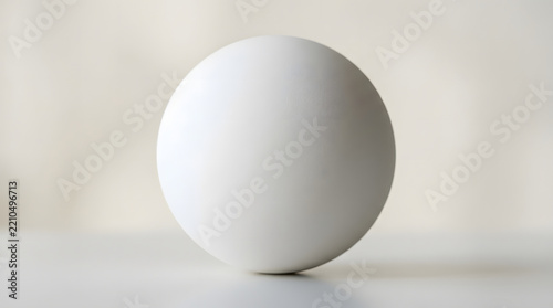 A minimalist white sphere with a smooth matte finish sits centered on a clean neutral surface in soft studio lighting.