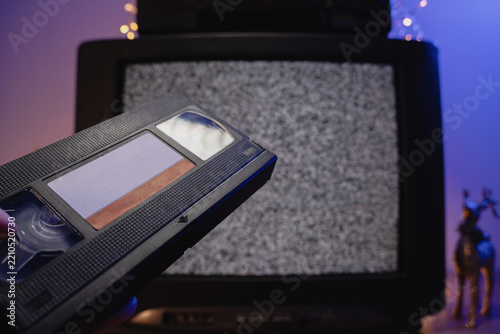 Hand holding VHS tape in front of old television static screen