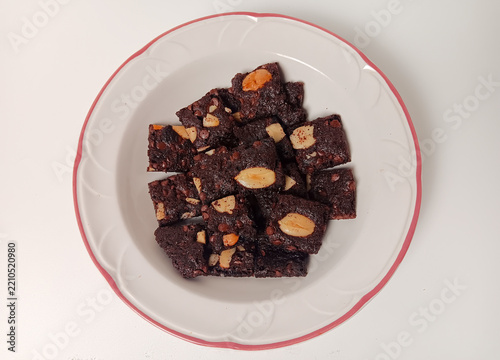 Homemade chocolate brownie crisps, topped with almond pieces and chocolate chips, served on a white plate isolated on white background.