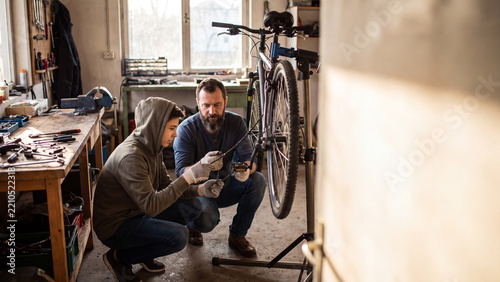 Father and teenage son repairing bicycle chain in garage workshop with blurred background banner.