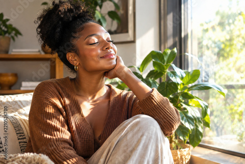 A beautiful young African American woman with curly hair smiles peacefully with closed eyes, enjoying a moment of tranquility and self-care