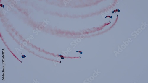 Parachute team floating in the sky with red smoke trails