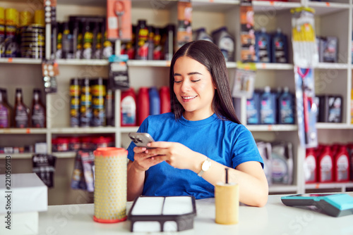 Smiling latin woman scanning auto parts with smartphone in a retail store