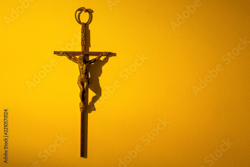 Metal crucifix hanging on a wall in warm yellow light with copy space.