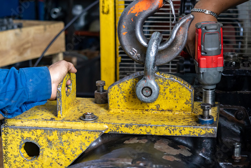 Mechanics secure heavy crane lifting bracket using cordless impact wrench inside repair workshop.