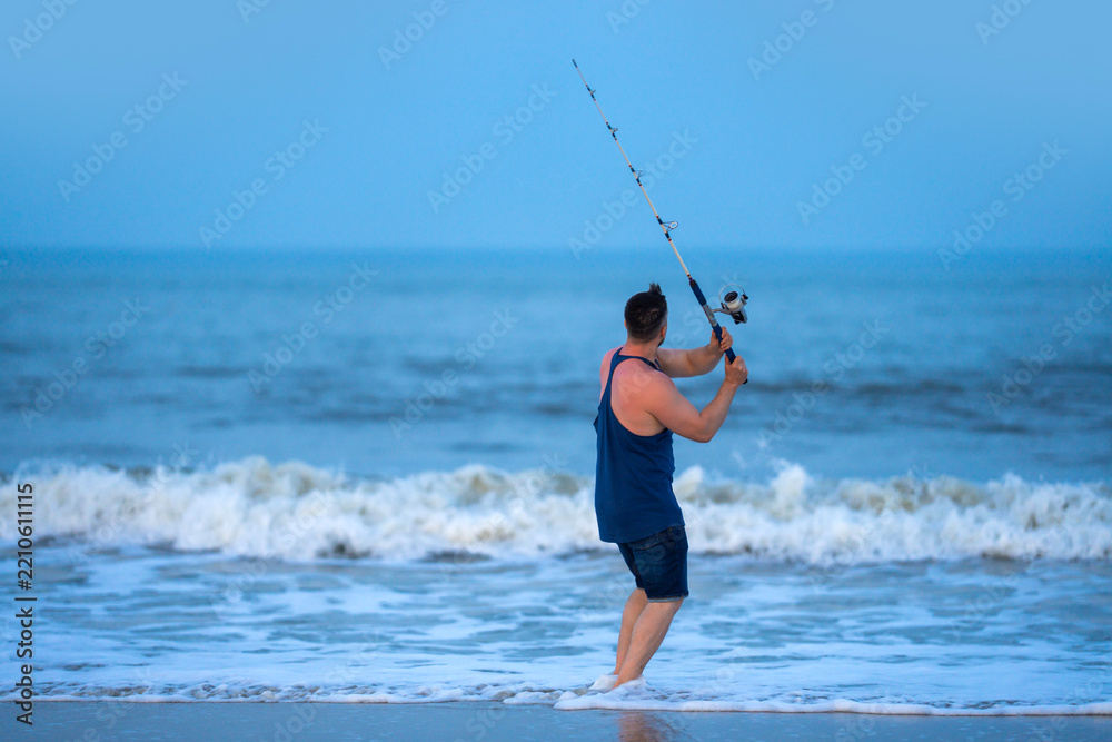 Fototapeta premium Sea fishing creates outdoor recreation. Sea fishing shows ocean lifestyle. Angler enjoys sea fishing on beach. Man practices sea fishing by surf.