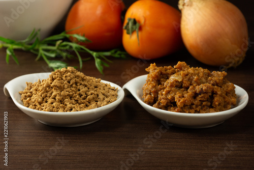 Side-by-side comparison in small white bowls showing textured soy protein in its raw, dry state on the left, and cooked and seasoned on the right, accompanied by fresh tomatoes and an onion 