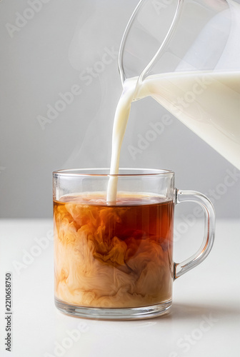 Pouring fresh milk into hot tea mug with swirl liquid effect and steam