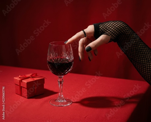Hand reaching for glass of red drink on a table with red cloth and small gift box