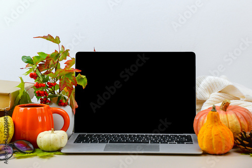 workspace with laptop, pumpkins, coffee cup, glasses and colorful fall leaves on a neutral desk with copy space.