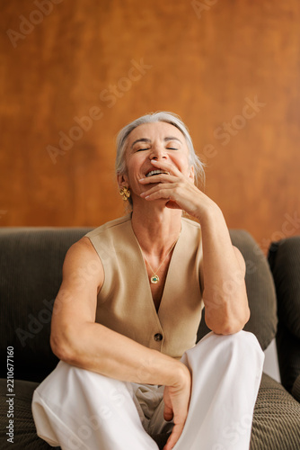 Mature woman laughing heartily on sofa experiencing genuine joy