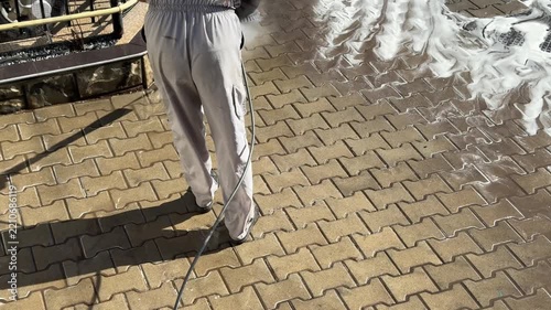 Worker pressure washing pavement with foam