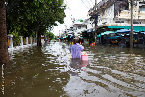 Back view, obese woman wearing Raincoat and walking through flood waters to go buy food, lifestyle of Thai people in massive flooding, Severe weather