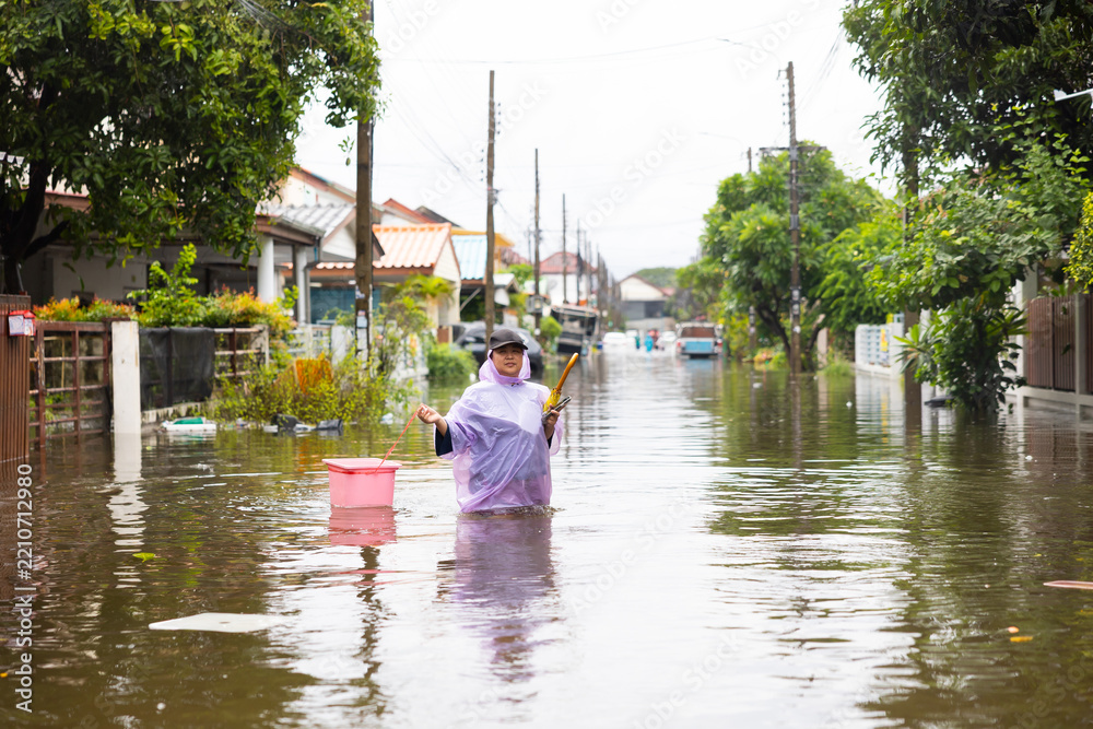Fototapeta premium obese woman wearing Raincoat and walking through flood waters to go buy food, lifestyle of Thai people in massive flooding, Severe weather