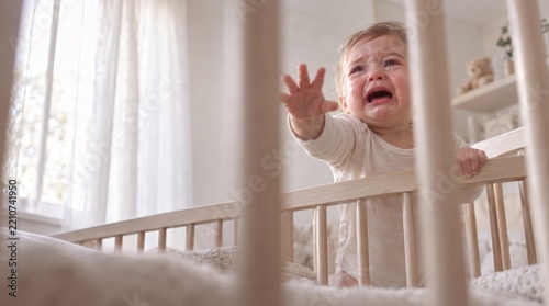Baby cries alone in a crib in a children's corner