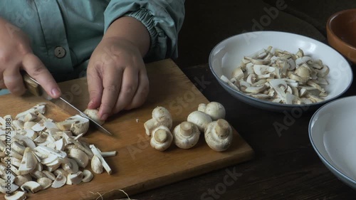 Cutting fresh champignons with a knife on a cutting board on a wooden table