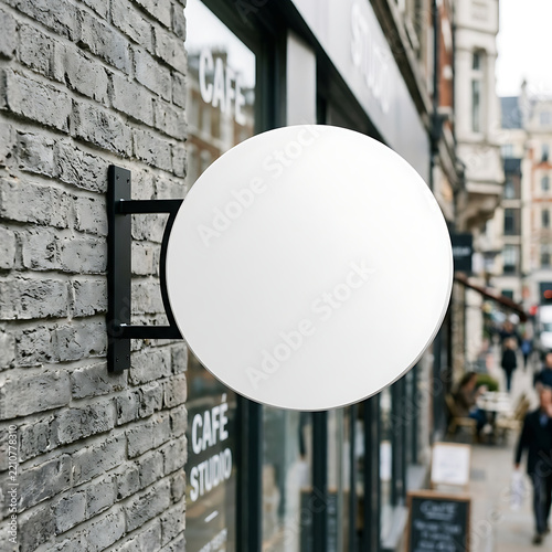 Empty circular cafe sign mounted on a textured brick exterior wall with a busy street visible in soft focus