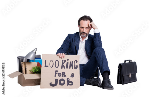 Full size photo of  loser fired worker mature guy business man jobless man hold placard need search work sit floor briefcase belongings box stuff wear suit shoes isolated grey background
