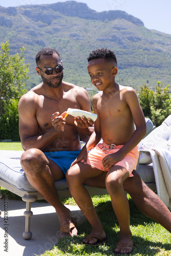 Fotografie African American father and child in swimwear sitting on chaise lounge at pool c