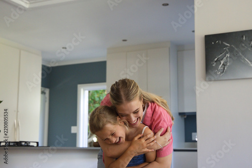 Mother and child hugging, leaning on kitchen counter by window wearing pink and blue tops