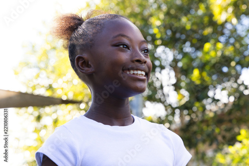 African American child smiling looking upward in park near railing wearing white shirt puff bun