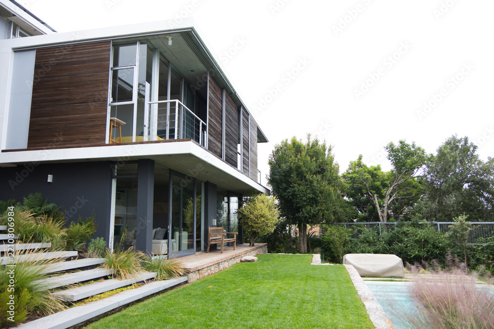 Obraz premium Modern two-story house is showing wood cladding and balcony over timber deck in suburban backyard