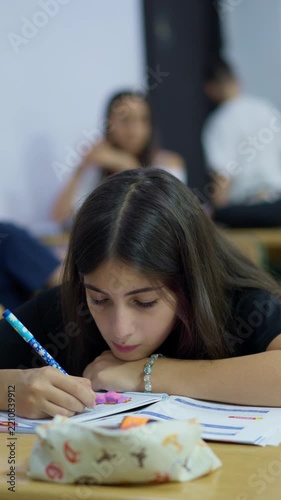 Focused student writing in a notebook during a classroom lesson with peers in the background