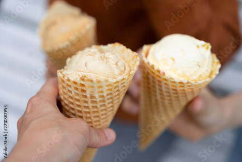Closeup of happy friends and companions enjoying sweet vanilla ice cream together outdoors on a warm summer day, celebrating friendship and togetherness while sharing a delicious treat.