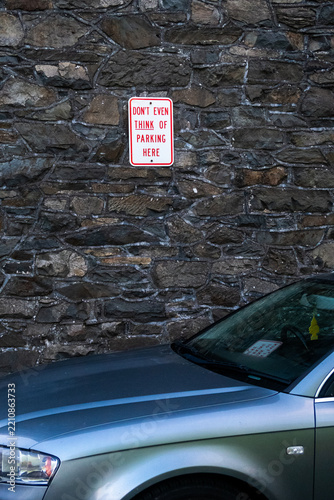 Silver car parked near stone wall with no parking sign visible