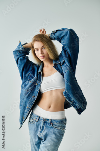 Young woman poses stylishly in contemporary denim fashion against a minimal backdrop