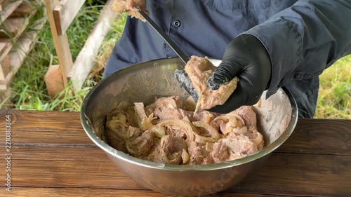 Close-up of hands in black gloves threading pieces of meat onto a skewer, outdoor cooking. High quality 4k footage