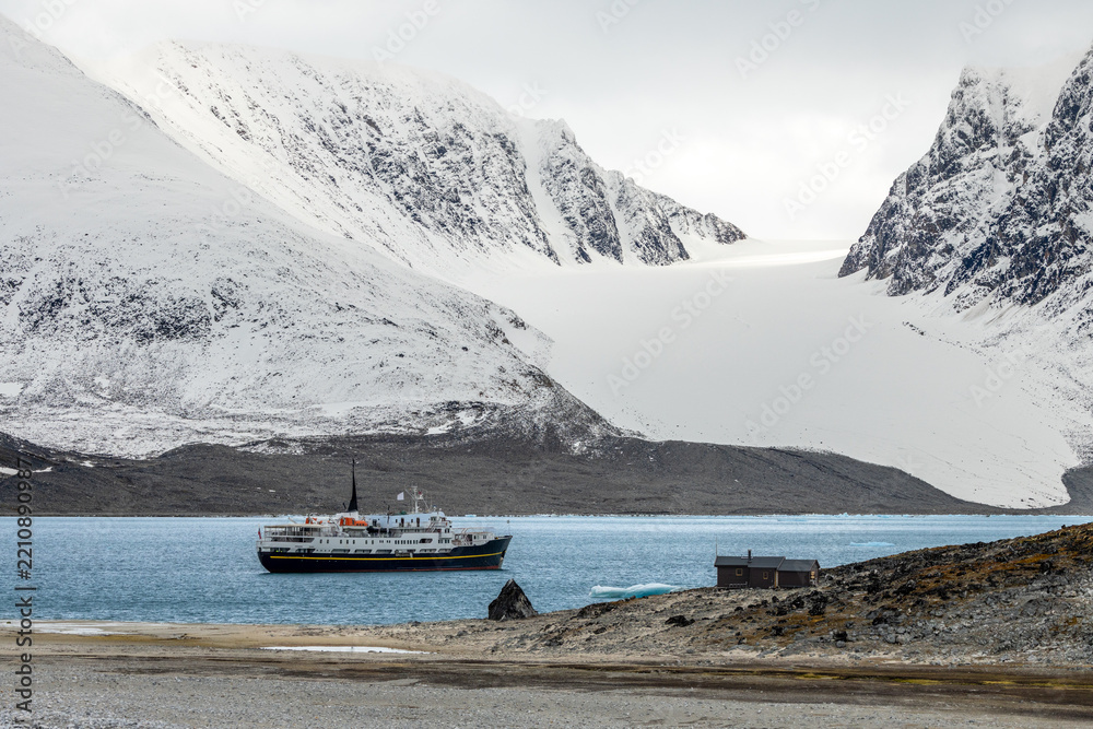 Fototapeta premium Remote summer Arctic landscape with ship, small cabin, blue fjord water and glacier framed by steep rugged mountains, Spitsbergen, Svalbard, Norway