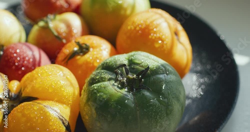 Yellow, green and red tomato on a dark plate. Tomatoes sprinkled with water. Agricultural industry and farming.	
