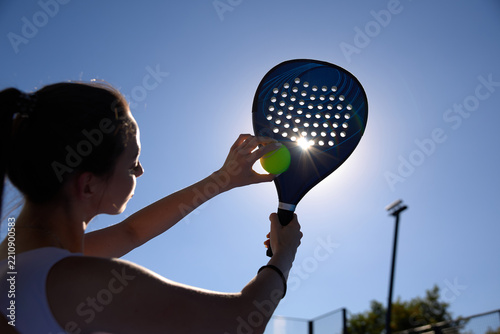 Obraz na plátně Backlit outdoor shot of a sportswoman holding a tennis ball against a perforated padel racket in bright sunlight