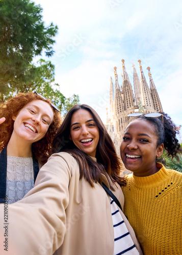 Vertical. Young only women friends taking selfie in front of Sagrada Familia, Barcelona. Beautiful mixed race girl on street of European city enjoying vacation happy and smiling. Funny tourism people