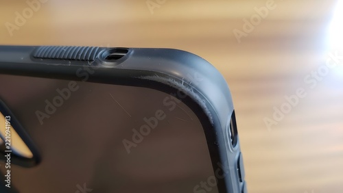 Close-up view of a damaged black smartphone protective case showing visible scratches and wear on the corner bumper over a wooden background