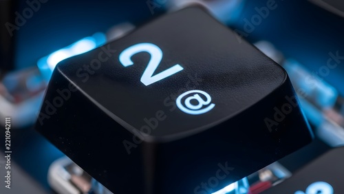 Close-up of a backlit keyboard key displaying the number '2' and the '@' symbol, representing digital communication and online presence