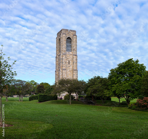 Tall historic stone carillon bell tower standing in a lush green urban park in Frederick, Maryland, under a striking blue sky with patterned clouds.
